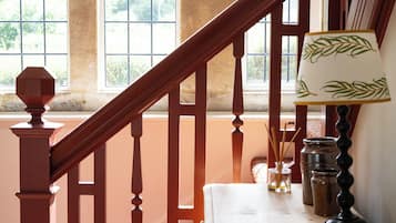 Uma escada de madeira com corrimão, uma mesa com abajur e uma janela com vista para vegetação.
