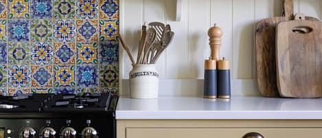 A kitchen with a patterned tile backsplash, a stove, wooden utensils, and a cutting board on the counter.