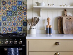 A kitchen with a patterned tile backsplash, a stove, wooden utensils, and a cutting board on the counter. - Costers Lodge (Midhurst)