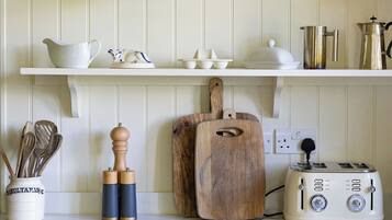 Una cocina con armarios blancos, una tabla de cortar de madera, un tostador antiguo y varios utensilios de cocina.