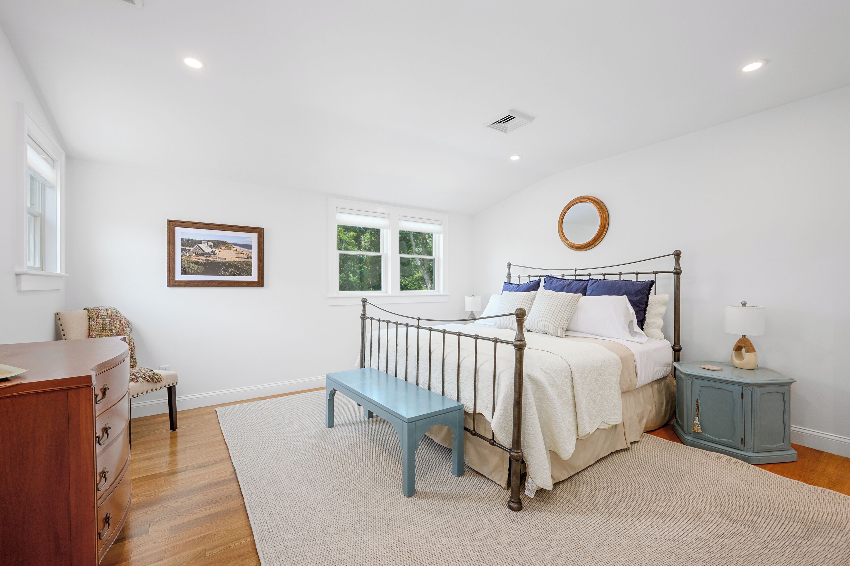Une chambre à coucher avec un lit, une table de chevet, une commode, une fenêtre et un tableau au mur.