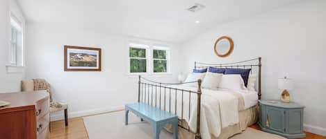 A bedroom with a bed, a bedside table, a dresser, a window, and a picture on the wall.