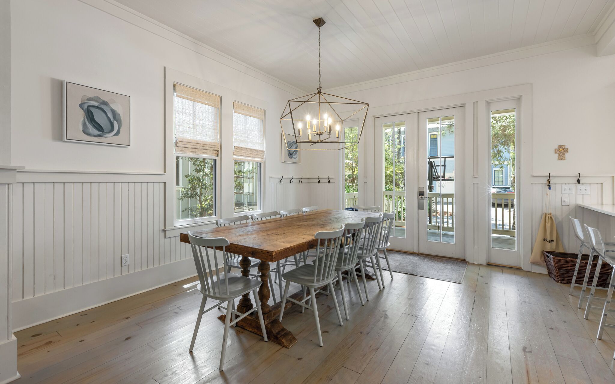 A dining area with a wooden table and white chairs, a chandelier, and a view through the glass doors.