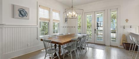 A dining area with a wooden table and white chairs, a chandelier, and a view through the glass doors.