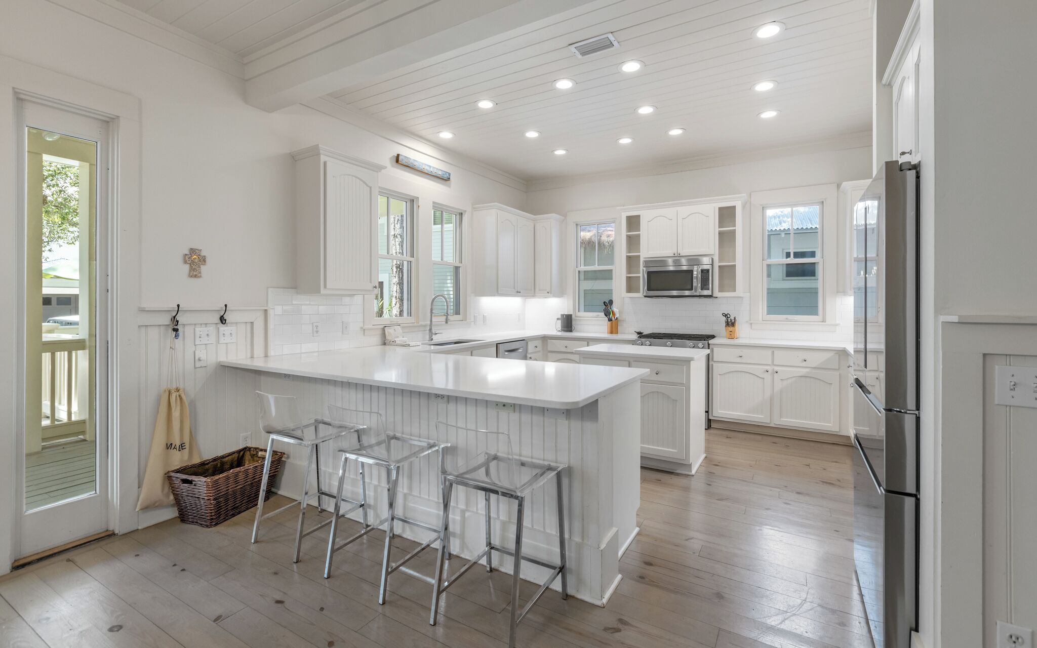 A spacious kitchen with white cabinetry, a large island with bar stools, and a stainless steel refrigerator.