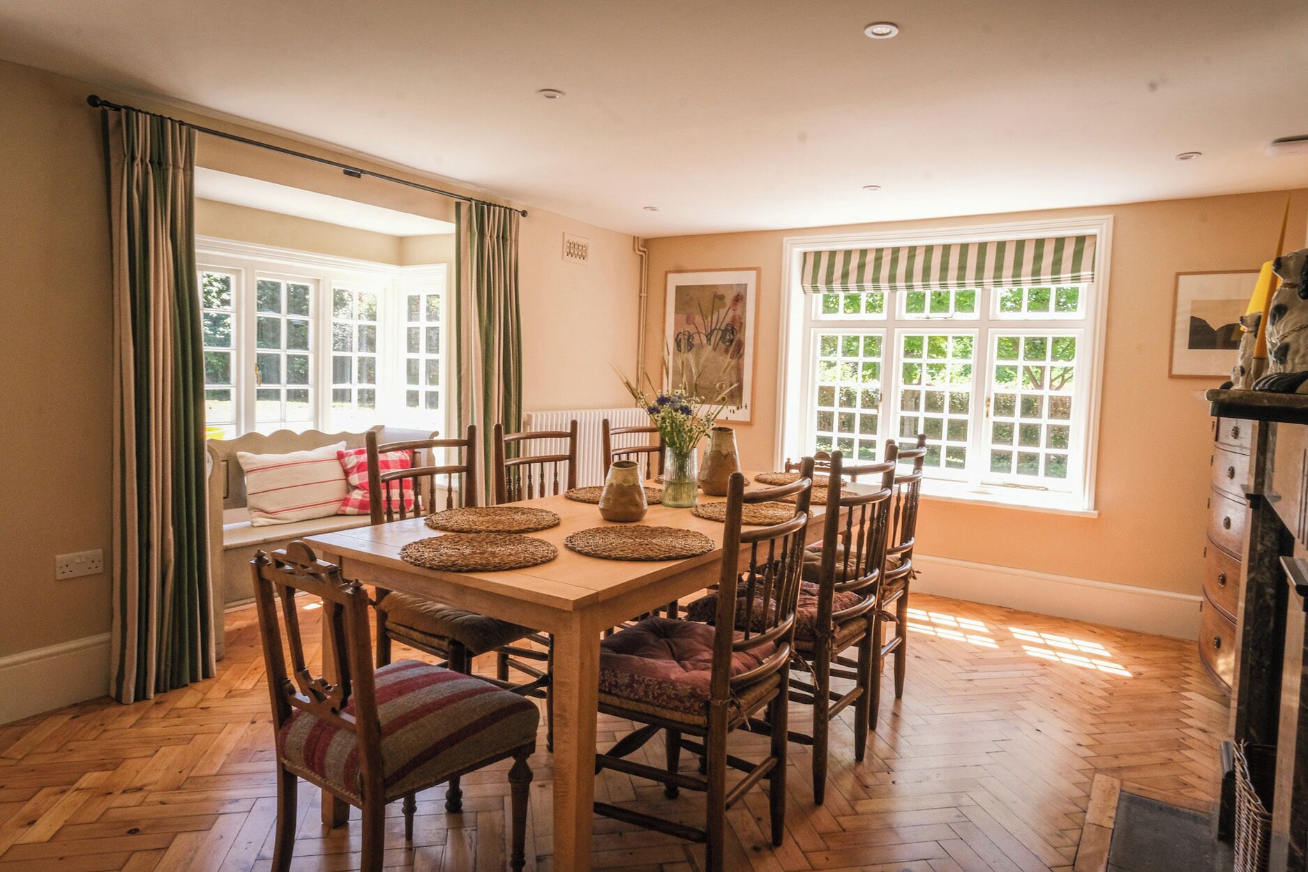 A dining area with a wooden table, chairs, and a view of the outdoors through large windows.