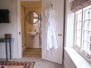 A bathroom with a white sink, a mirror, and a white bathrobe hanging on the door.