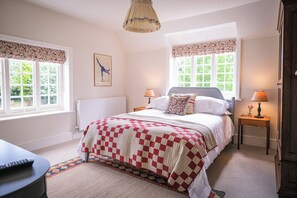 A bedroom with a bed, two bedside tables, a lamp, a radiator, and a window with a view of greenery.