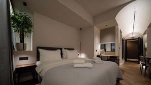 A modern hotel room with a large bed, a desk, a chair, and a potted plant.