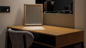 A wooden desk with a chair, a framed mirror, and a black device on the wall.