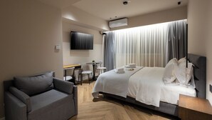 A modern hotel room with a bed, a sofa, a desk, and a TV.