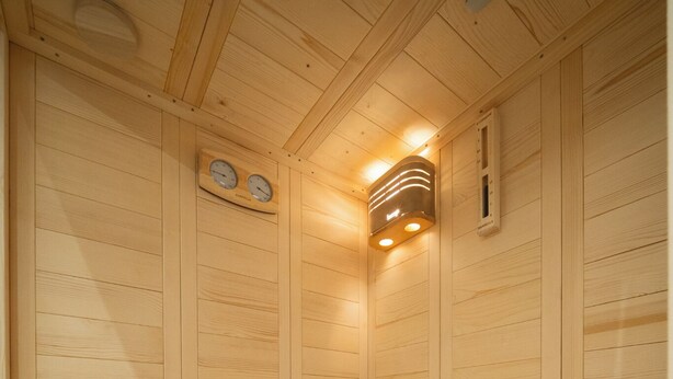 A sauna with wooden walls, a bench, a bucket, and a stone heater.