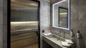 A modern bathroom with a glass door, a large mirror, and two sinks with soap dispensers.