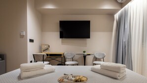 A hotel room with a bed, a flat-screen TV mounted on the wall, a desk with two chairs, and a small table with a plant.