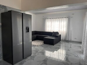 A modern kitchen with a built-in refrigerator, a dark-colored sectional sofa, and a patterned rug.
