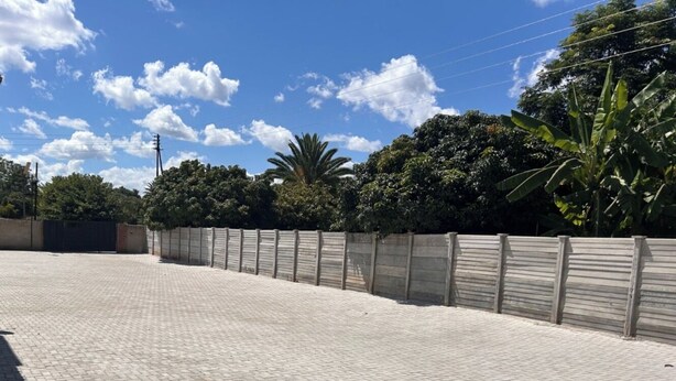 Un espacio exterior empedrado con diseño de ladrillo, rodeado por una cerca de madera y abundante vegetación.