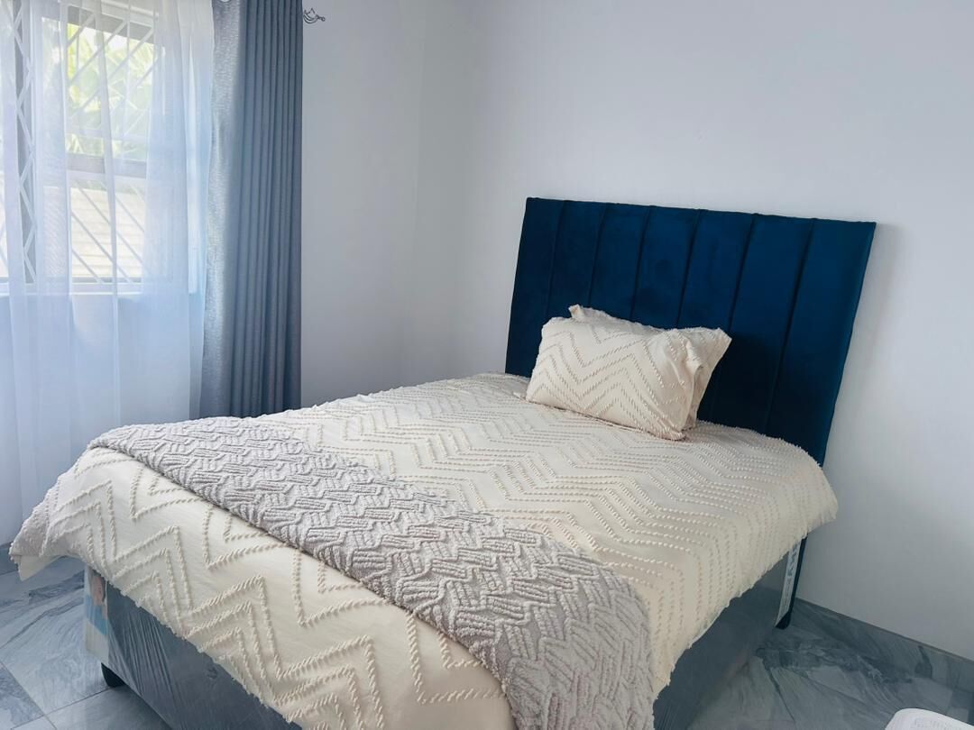 Ein Bett mit blauer Kopfteil, einer beige karierten Tagesdecke und einem Kissen.
