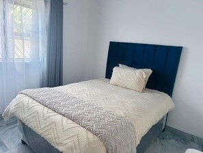Una cama con cabecera azul, una colcha de color beige con estampado y una sola almohada.
