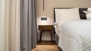 A hotel room with a bed, a bedside table, a nightstand, and a wall-mounted control panel.