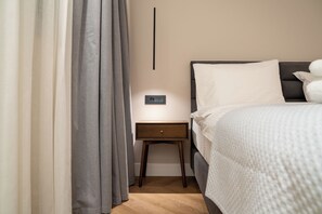 A hotel room with a bed, a bedside table, a nightstand, and a wall-mounted control panel.