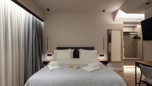 A modern hotel room with a large bed, bedside tables, a mirror, and a view into the bathroom.