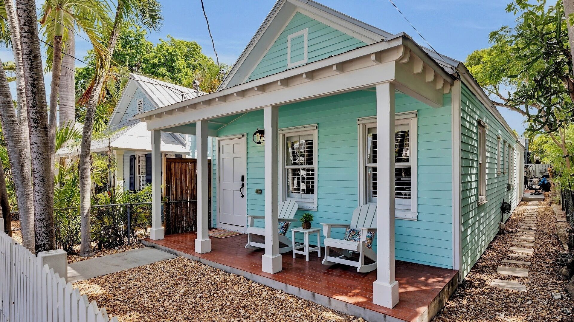A turquoise house with a porch, white columns, and a small garden area.
