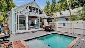 Ein zweistöckiges Haus mit Pool, Gartenmöbeln und einem weißen Zaun.