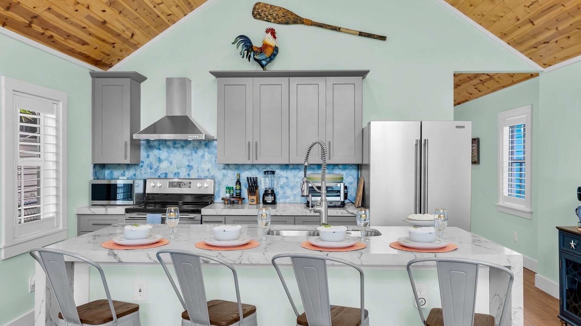 A modern kitchen with a central island, stainless steel appliances, and a decorative rooster.