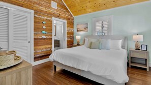 Een slaapkamer met een houten plafond, een bed met wit beddengoed, twee nachtkastjes met lampen, en een muur met een decoratie in maritieme stijl.
