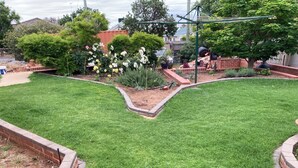 Une pelouse bien entretenue bordée de briques, un jardin avec différentes plantes et fleurs, et un ensemble de jeux pour enfants avec une balançoire.