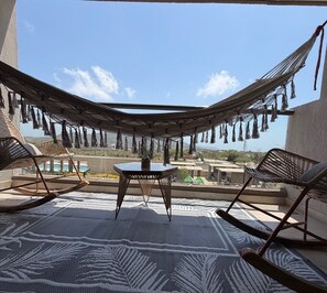 A hammock chair, a table, and a view of a pool and buildings.