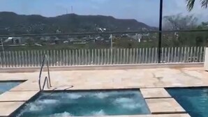 Piscina con una cascada, rodeada por una valla de madera y vistas a colinas distantes.