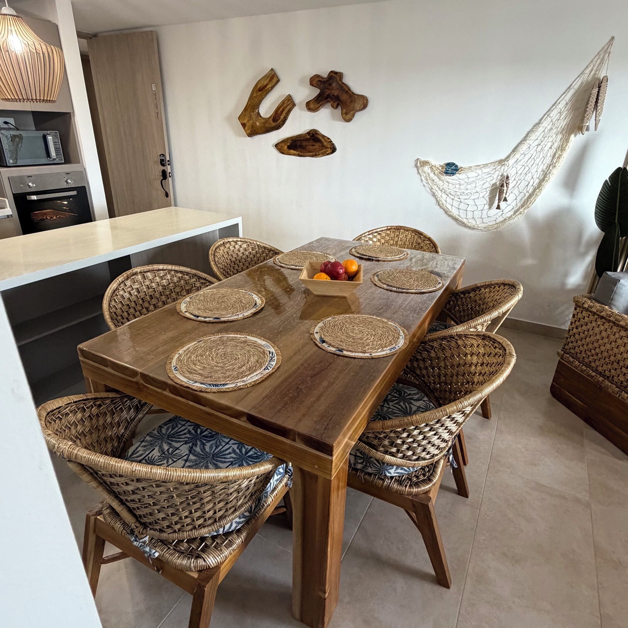 Een eetgedeelte met een houten tafel, gevlochten stoelen en een hangmat.
