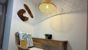 Una silla de mimbre con cojín, un escritorio de madera, una lámpara colgante y adornos en la pared.