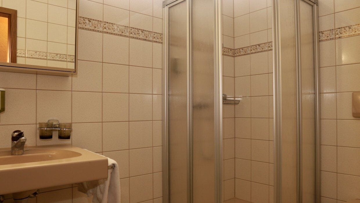 A bathroom with a sink, mirror, and shower enclosure.