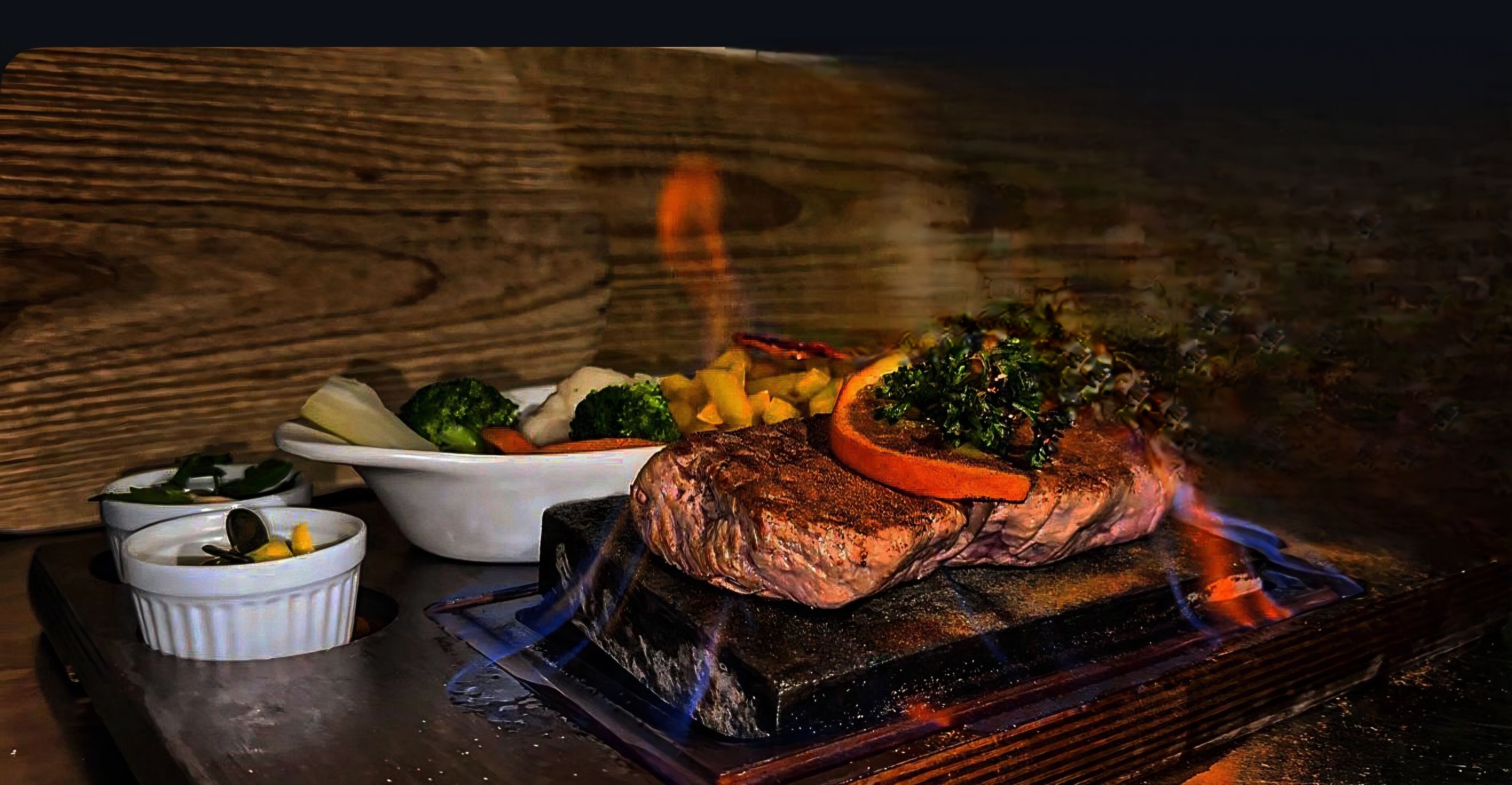 Un plato de carne con vegetales, un bol de papas y un recipiente pequeño de salsa.