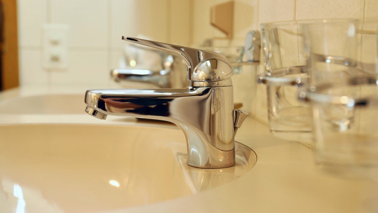 A modern bathroom sink with a chrome faucet and clear glass drinking glasses.