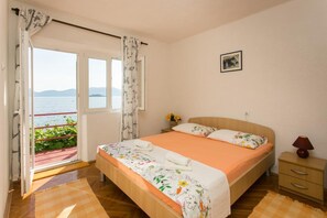 A bedroom with a bed, a nightstand, a lamp, a picture on the wall, and a view of the sea through a window. - Apartments Stipo - Comfort Two Bedroom Apartment With Balcony and Sea View (Janjina)
