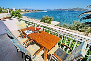 A wooden table with chairs on a balcony overlooking a coastal area with a clear view of the sea and distant mountains. - Apartments Stipo - Comfort Two Bedroom Apartment With Balcony and Sea View (Janjina)