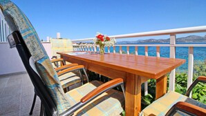 A wooden table with chairs and a vase of flowers, set against a backdrop of a clear blue sky and a body of water. - Apartments Stipo - Comfort Two Bedroom Apartment With Balcony and Sea View (Janjina)