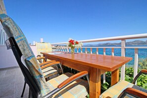 A wooden table with chairs and a vase of flowers, set against a backdrop of a clear blue sky and a body of water. - Apartments Stipo - Comfort Two Bedroom Apartment With Balcony and Sea View (Janjina)