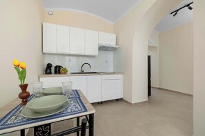 A compact kitchen with white cabinets, a built-in oven, and a sink. There's a dining table with a vase of flowers and a bowl of fruit. - Stylish Apartment in Bielsko-Biala | Near the Town Hall (Bielsko-Biała)