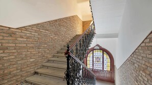 Una escalera con un muro de ladrillo a un lado y un muro blanco al otro, que conduce a una habitación con un vitral.
