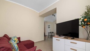 A living room with a red sofa, a flat-screen TV on a white cabinet, and a dining area with a table and chairs. - Practical Studio for a Business Stay | Close to the City Centre (Bielsko-Biała)