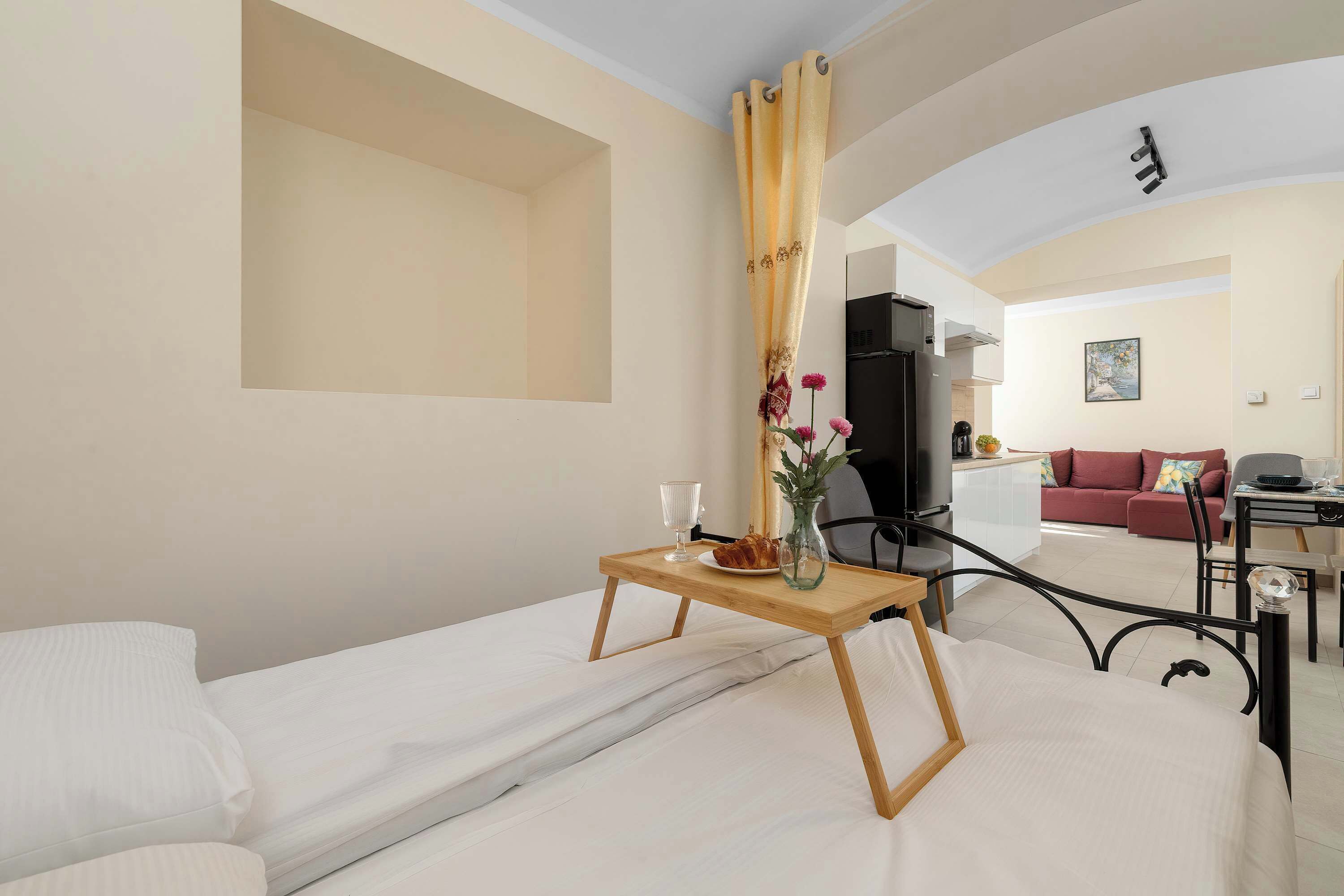 Een hotelkamer met een bed, een klein tafeltje met een vaas en een bord, een televisie en een rode bank op de achtergrond.