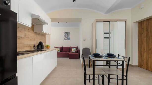 A modern kitchen with white cabinets, a black refrigerator, and a wooden countertop. There is a dining area with a table and chairs, and a red sofa in the background. - Practical Studio for a Business Stay | Close to the City Centre (Bielsko-Biała)