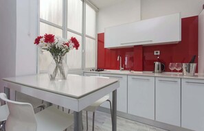 A modern kitchen with white cabinets, a glass table, and a vase of flowers. - Red Gordon Beach View Apartments + Bomb Shelter (Tel Aviv-Yafo)