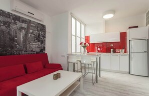 A modern apartment with a red sofa, a white dining table, and a kitchen with white cabinets and a red accent wall. - Red Gordon Beach View Apartments + Bomb Shelter (Tel Aviv-Yafo)