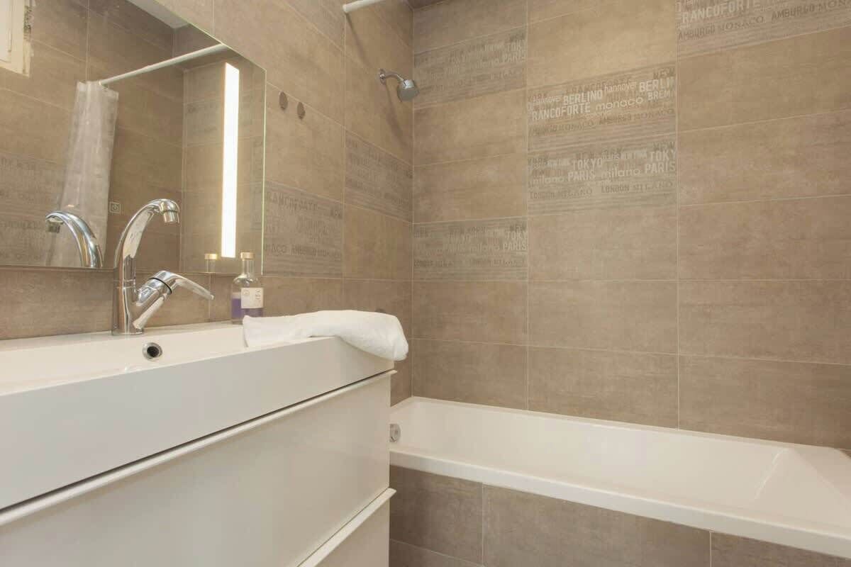 Un baño con tocador blanco, espejo, ducha y paredes de azulejos color beige.