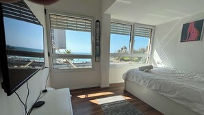 Ett sovrum med en säng, ett skrivbord, en tv och stora fönster med utsikt över havet.